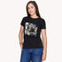 A woman with long brown hair wears SUZI ROHER’s The Niki—a 100% cotton black crew neck T-shirt featuring a collage of classic cinema scenes and “cinema”—standing with one hand in her jeans pocket against a plain background.