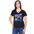 A woman with long brown hair, wearing SUZI ROHER's The Viv black V-neck T-shirt featuring a colorful Love Soul Color graphic and blue jeans, stands with one hand on her hip against a white background.