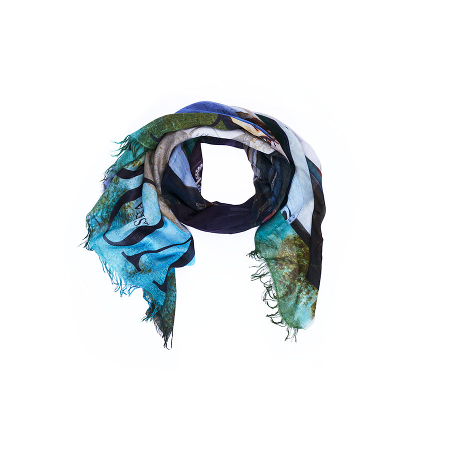 The “Lily, Spanish Vogue” scarf by SUZI ROHER features a soft blend of blue, green, and brown hues in a loose circular arrangement with frayed edges, displayed on a white background. Digitally printed from original artwork, this piece embodies the essence of contemporary Uruguayan fashion.