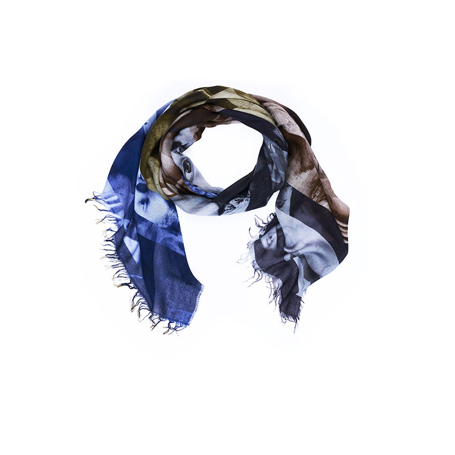 A loosely coiled SUZI ROHER Lily, Euphoria scarf with frayed edges, showcasing a mix of blue, brown, beige, and black abstract patterns inspired by original artwork, displayed on a white background.