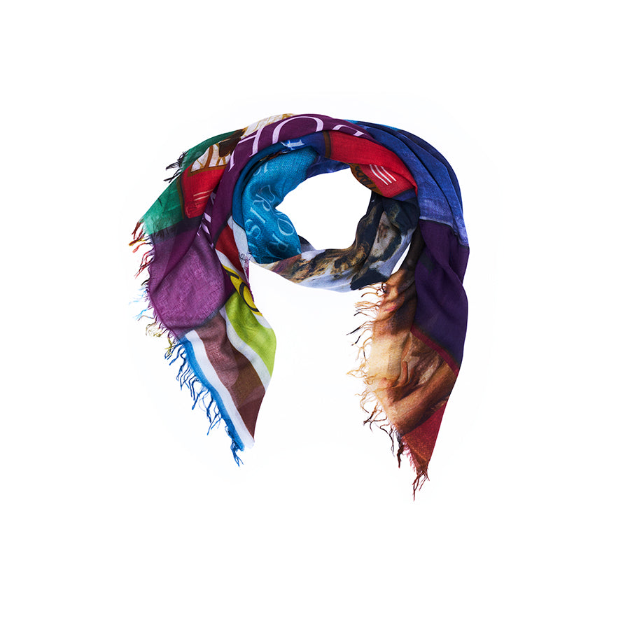 A vibrant rectangular scarf by SUZI ROHER, the “Lily, Opera,” features digitally printed original artwork in bold shades of blue, green, red, purple, and yellow with frayed edges. The scarf’s abstract pattern is beautifully showcased as it drapes in a loose loop against a white background.