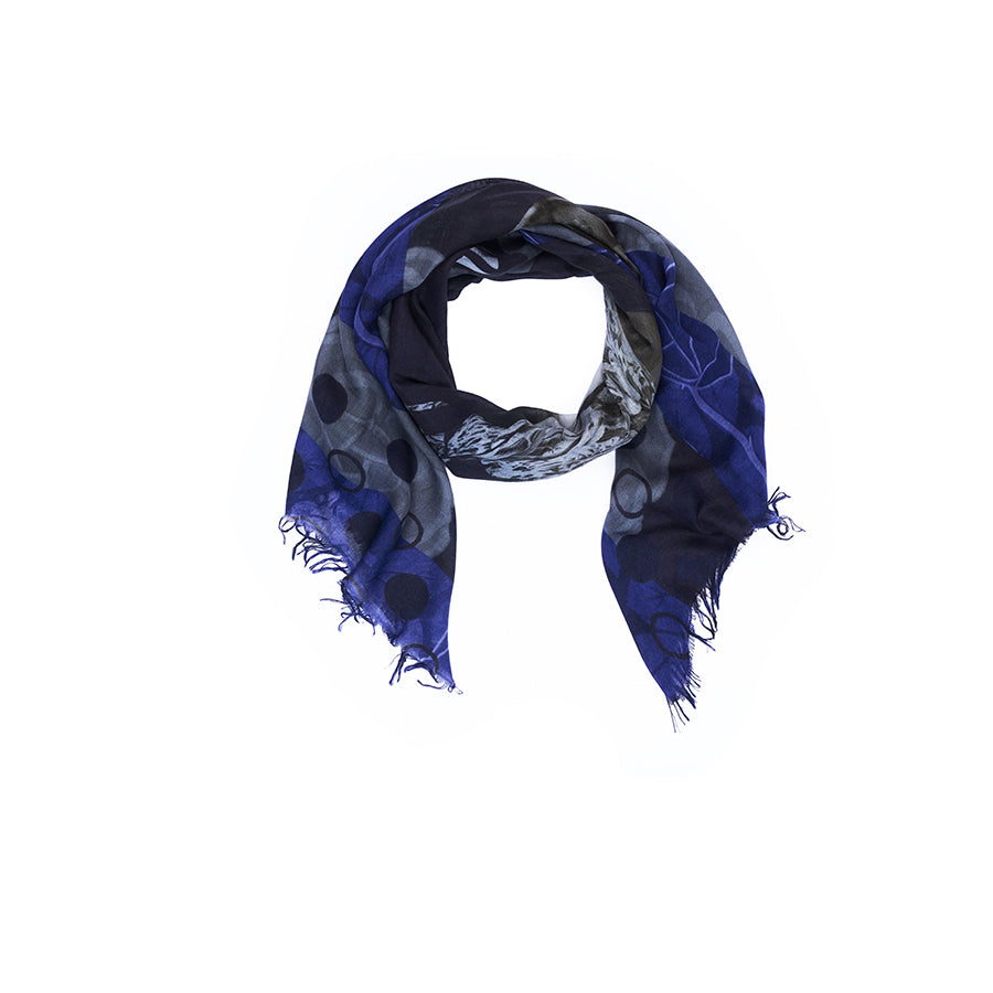 The Lily, Style Icon scarf by SUZI ROHER, featuring blue and gray tones with circular patterns and frayed edges, is displayed on a white background—an ideal accessory to channel a tomboy vibe when paired with classic trousers in iconic Katharine Hepburn style.