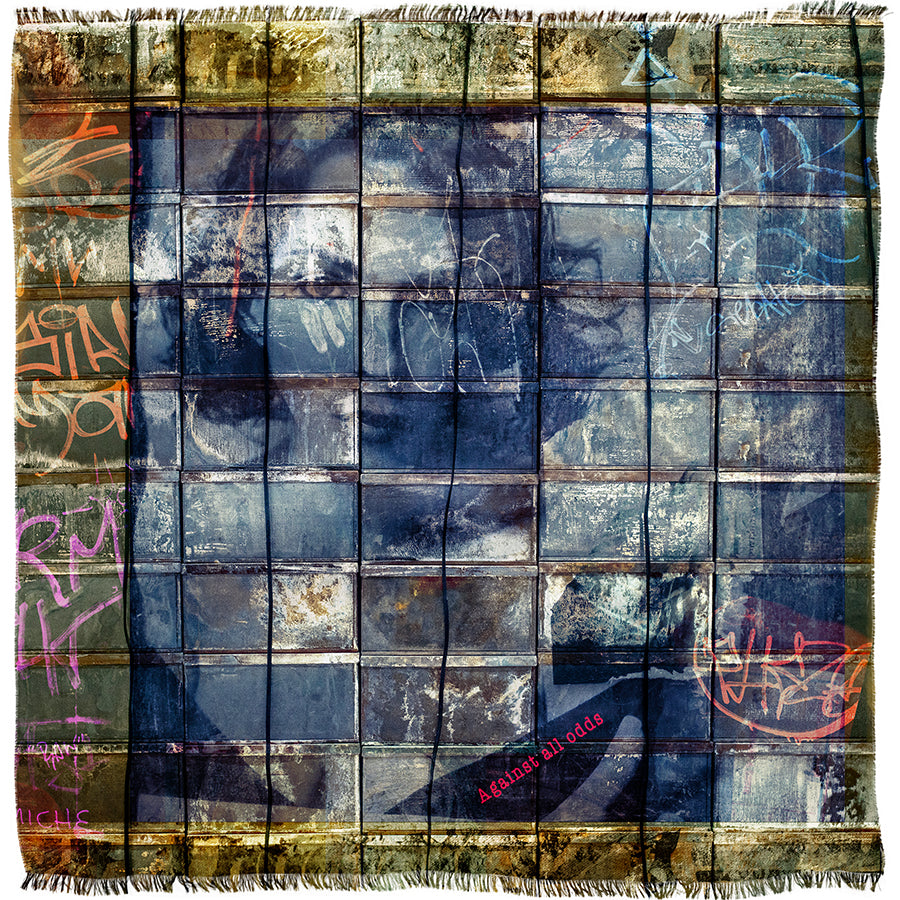A grid of weathered, square tiles adorned with colorful graffiti and scribbles reveals the faint suggestion of a face behind them. In the corner, a small red label features the words “Against All Odds” by SUZI ROHER.