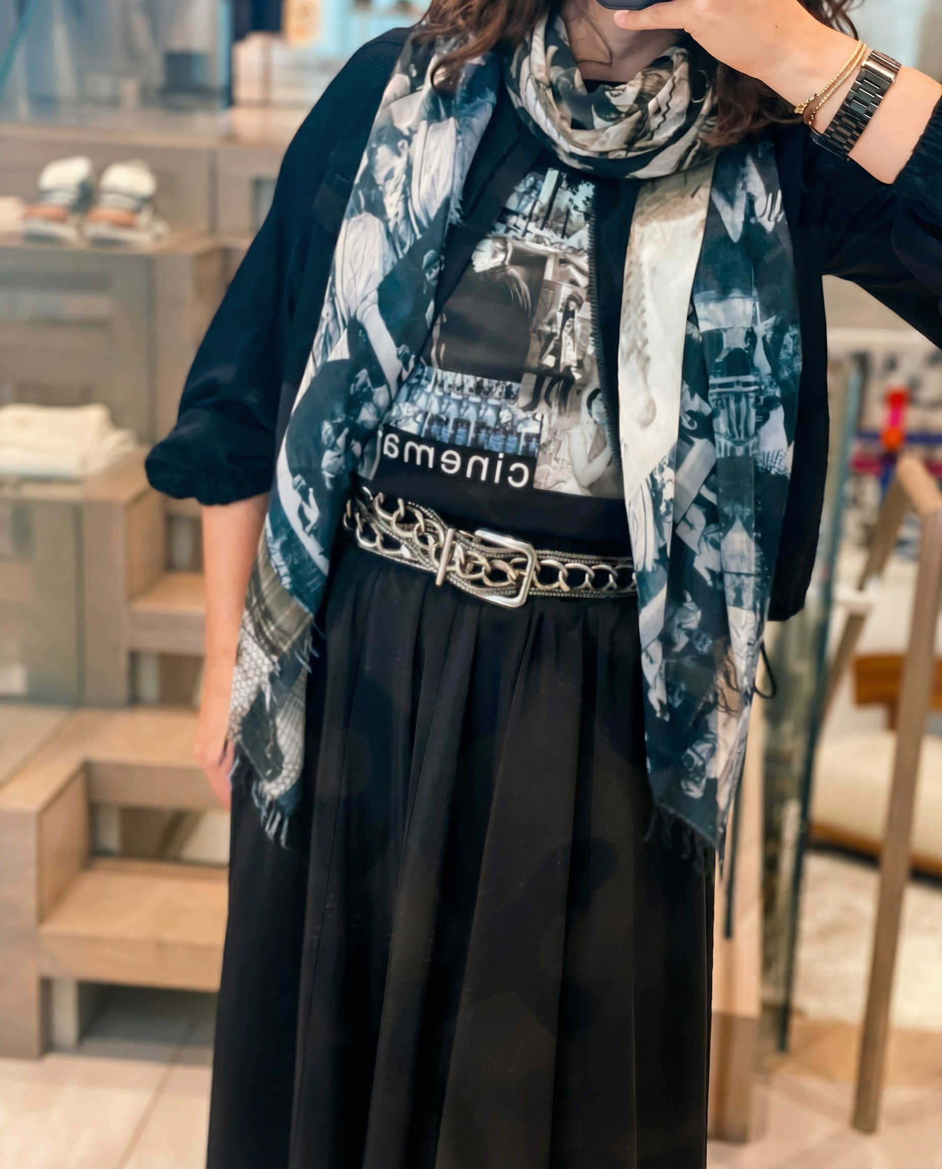 Person wearing a black dress with a patterned navy and black cinimatic scarf and belt in an indoor setting