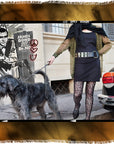 A woman in a black dress and patterned tights walks a large, shaggy black dog down a city street. Behind her is a mural featuring SUZI ROHER’s James Bond and other street art symbols.