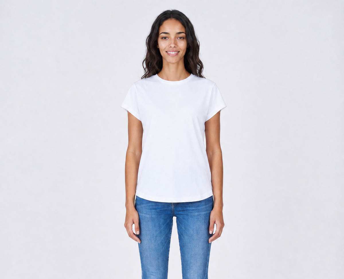 A woman with long dark hair stands smiling, wearing The KARLIE Tee By You customizable white t-shirt by SUZI ROHER and blue jeans against a light gray background.