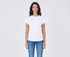 A woman with long dark hair stands smiling, wearing The KARLIE Tee By You customizable white t-shirt by SUZI ROHER and blue jeans against a light gray background.