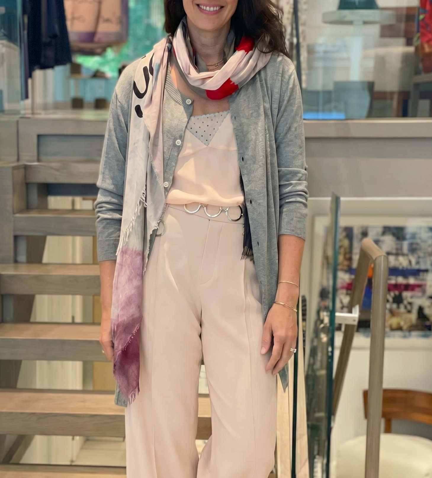 Woman wearing a light pink blouse and pants, and the "Love You Always" scarf by SUZI ROHER, showcasing an abstract floral pattern in black, gray, pink, red —a meaningful gift for any occasion. She is in an indoor setting.