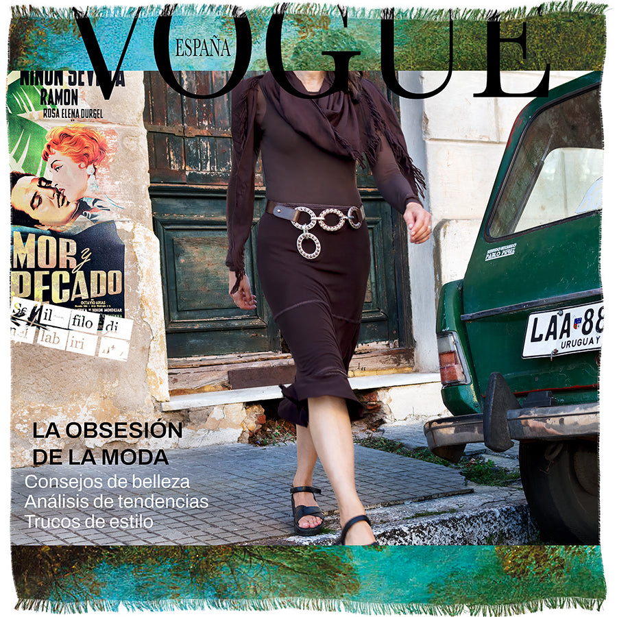 A woman in a brown dress and sandals walks past a green car and vintage posters on a weathered street, her image transformed into original artwork with an elegant Italian finish by SUZI ROHER, featured on the cover of Spanish Vogue.
