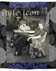 A black-and-white photo of a woman seated in a chair, overlaid with the text “Style Icon,” framed by a blue and gray floral patterned border; featuring the “Lily, Style Icon” art piece by SUZI ROHER.