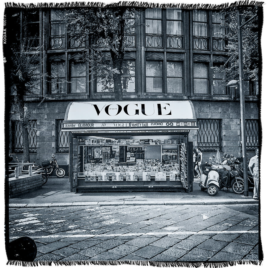Black-and-white photo titled “Vogue Italia B&amp;W” by SUZI ROHER, featuring a street newsstand with a prominent VOGUE sign, surrounded by parked scooters and motorcycles in front of an old building with tall windows and intricate architectural details.
