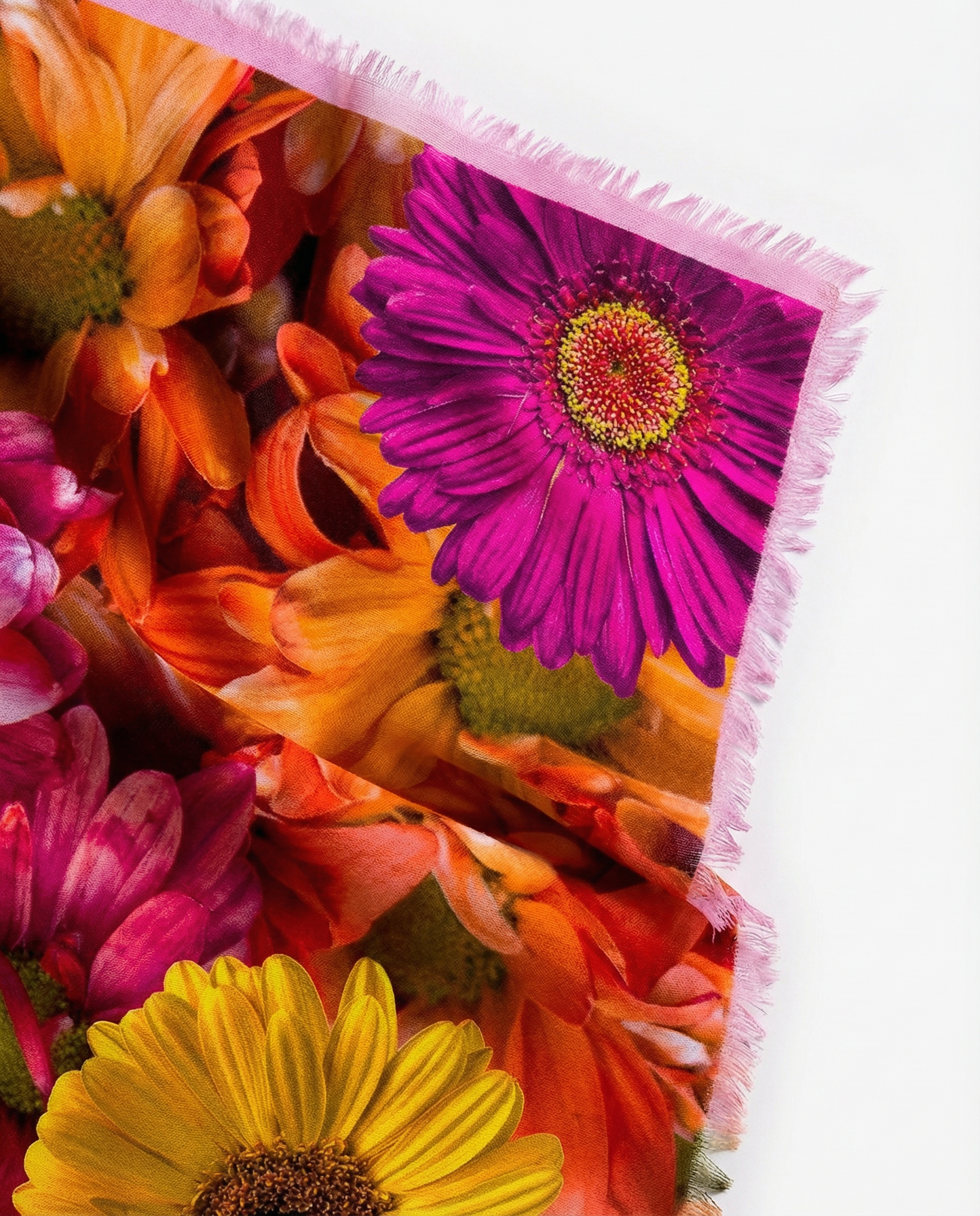 The soft drape of a large square scarf, showing bright pink, yellow, red flowers. Looks soft, and can see the fringe. 