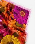 The soft drape of a large square scarf, showing bright pink, yellow, red flowers. Looks soft, and can see the fringe. 