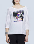 A woman wears SUZI ROHER’s The Bailey, a white boxy tee with three-quarter sleeves, featuring a colorful pop art woman’s face and the words BIZARRE and ART. She pairs it with black pants and a silver bracelet.