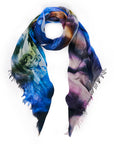 The SUZI ROHER "Love Is All We Need" scarf is a colorful Modal Silk accessory with an abstract design in blue, purple, yellow, and green hues with fringed edges, displayed in a loose loop on white. Made in Italy.