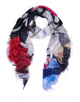 The SUZI ROHER "In The Details" scarf is lightweight and textured with frayed edges, showcasing an abstract black, white, red, tan, and blue pattern. Shown loosely looped on a white background.