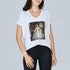 A woman wears SUZI ROHER’s The Velvet, a white oversized V-neck T-shirt featuring a historical woman in a lavish gown on the front, paired with black pants.