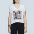 A woman wears SUZI ROHER’s "The Velvet"—a white V-neck tee featuring colorful abstract patterns and graffiti-style "I love you" motifs—paired with black pants and a silver bracelet, making it a perfect romantic gift.