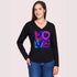A woman with long brown hair wears The Victoria black slim fit V-neck tee by SUZI ROHER, featuring a colorful LOVE graphic on the front, paired with blue jeans against a plain light background.