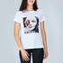 A woman with shoulder-length brown hair smiles in SUZI ROHER's The Niki tee, a classic 100% cotton white shirt featuring a black-and-white Audrey Hepburn portrait partly covered by a red heart and abstract designs.