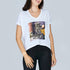 A woman wears The Velvet by SUZI ROHER—an oversized white V-neck tee with an abstract graphic and handwritten text: "It feels great to love and to feel with open heart and spirit. It feels great. Hot love," standing against a plain background.
