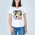 A woman models The Viv by SUZI ROHER—a slim fit, 100% cotton white V-neck tee featuring a vibrant collage of magazine covers and photos—paired with blue jeans against a plain light background.
