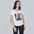 Woman with long brown hair wears SUZI ROHER’s The Viv graphic cotton t-shirt and black pants, standing against a light gray background, looking at the camera with a slight smile.